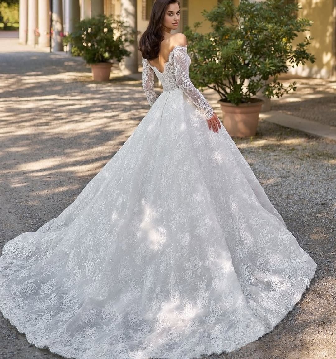 Elegant off-shoulder lace wedding gown with long sleeves and dramatic cathedral train in Italian courtyard — Sima Couture | Endless UAE