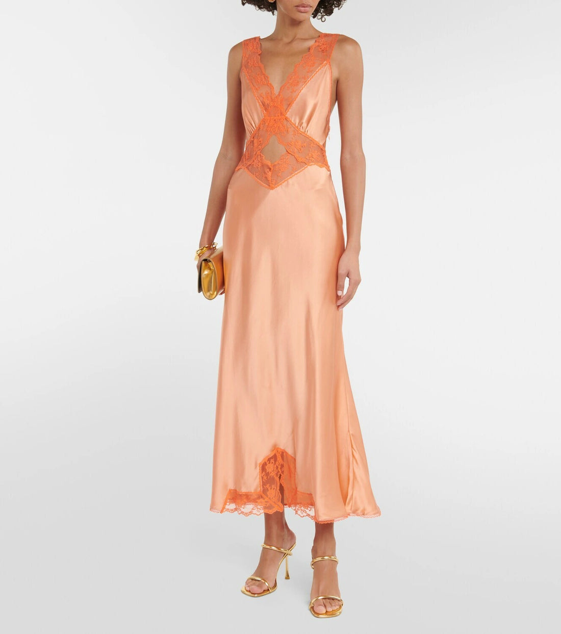Woman wearing Aries Cut Out Gown in orange peach with lace details and gold sandals — Sir The Label | Endless UAE