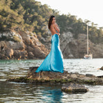 Woman in turquoise backless maxi dress standing on rocks by water at sunset — By Keara | Endless UAE
