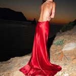 Elegant red satin backless maxi dress with cowl back and flowing train at sunset — By Keara | Endless UAE