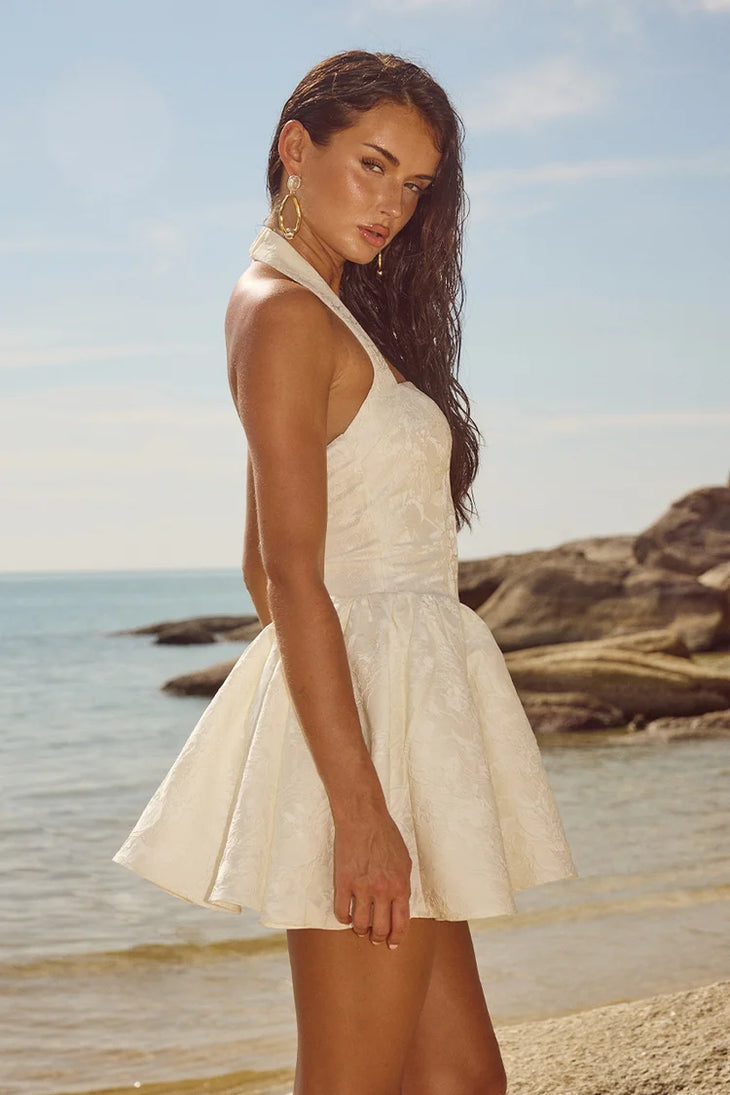 Sabine Mini Dress in cream with halter neckline and textured fabric on beach — Runaway The Label | Endless UAE