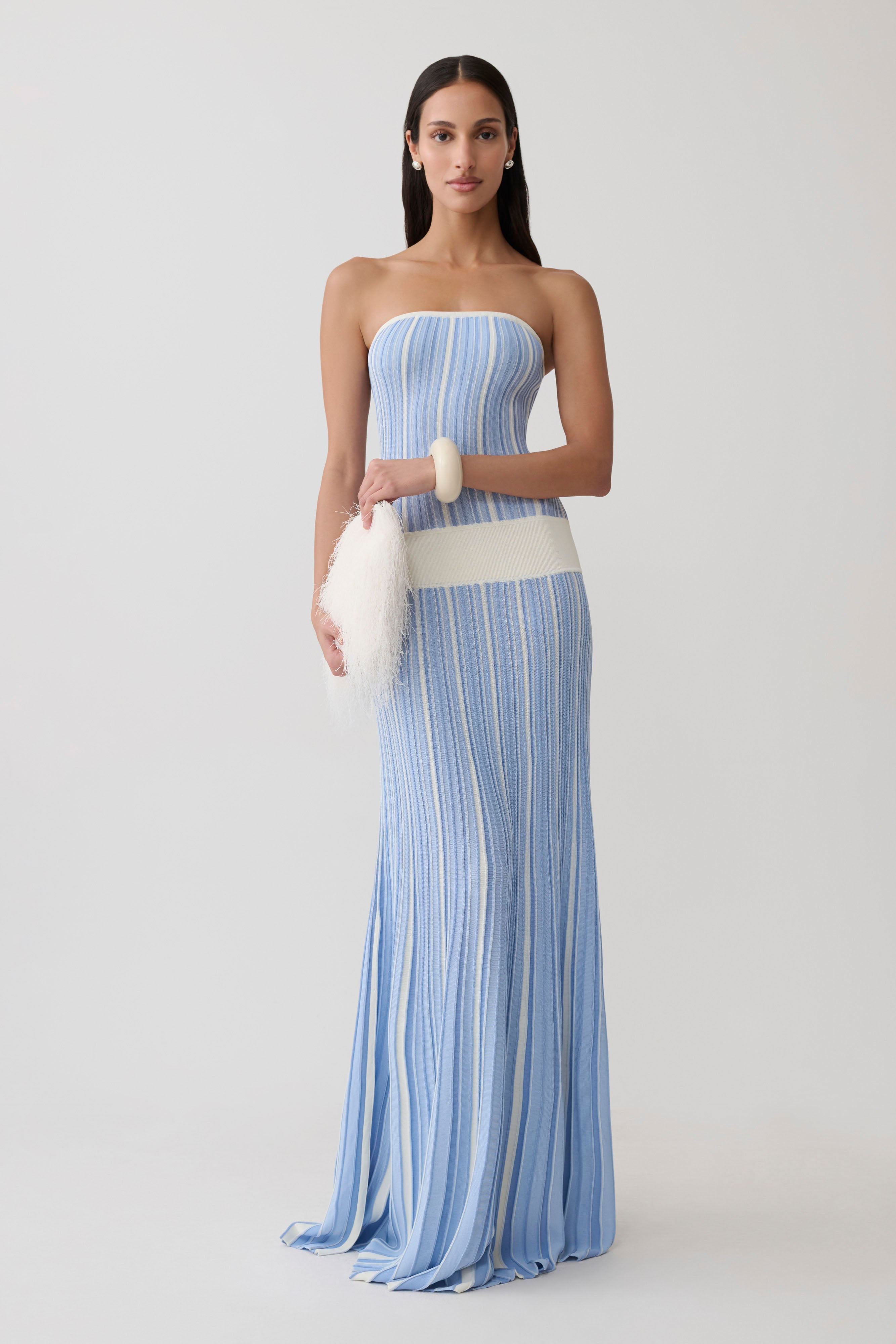 Woman wearing light blue striped strapless maxi knit dress with cream belt and white clutch — Meshki | Endless UAE