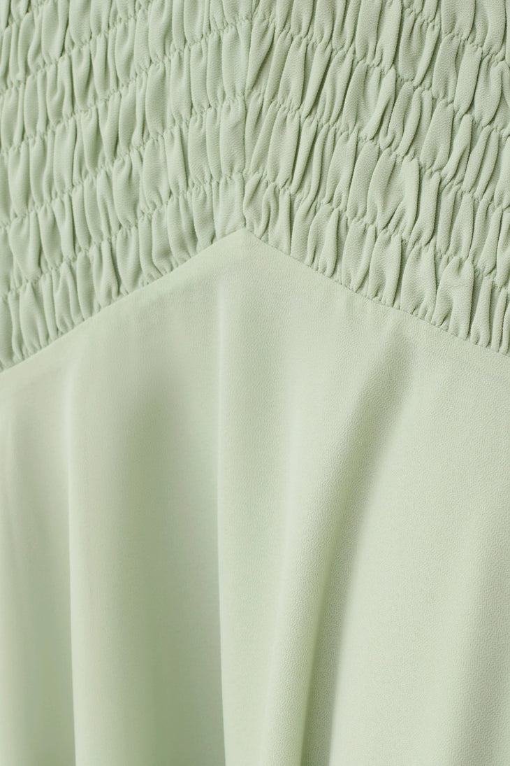 Woman wearing pale green halterneck maxi dress with shirred bodice and asymmetrical hem — Meshki | Endless UAE