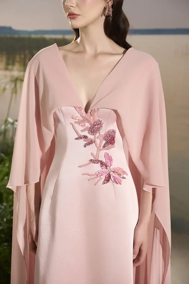 Woman wearing blush pink flowing gown with floral embellishment and draped cape at lakeside sunset — Tracy Studio | Endless UAE