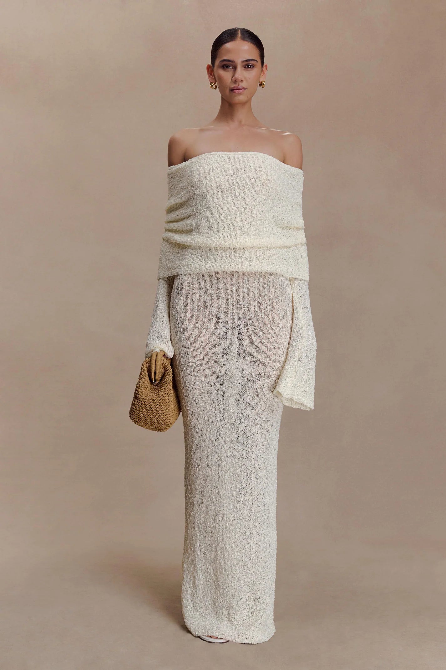 Woman wearing cream off-shoulder boucle maxi dress with draped sleeves and gold woven handbag — Meshki | Endless UAE