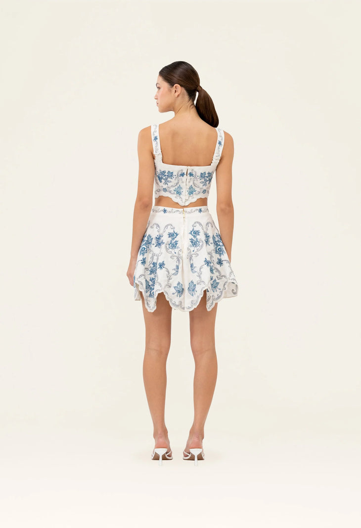 Woman wearing white cropped top and scalloped skirt with blue floral embroidery — Agua by Agua Bendita | Endless UAE