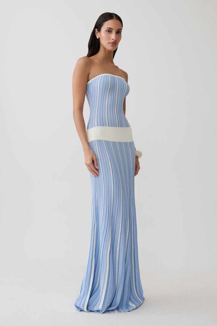 Woman wearing light blue striped strapless maxi knit dress with cream belt and white clutch — Meshki | Endless UAE