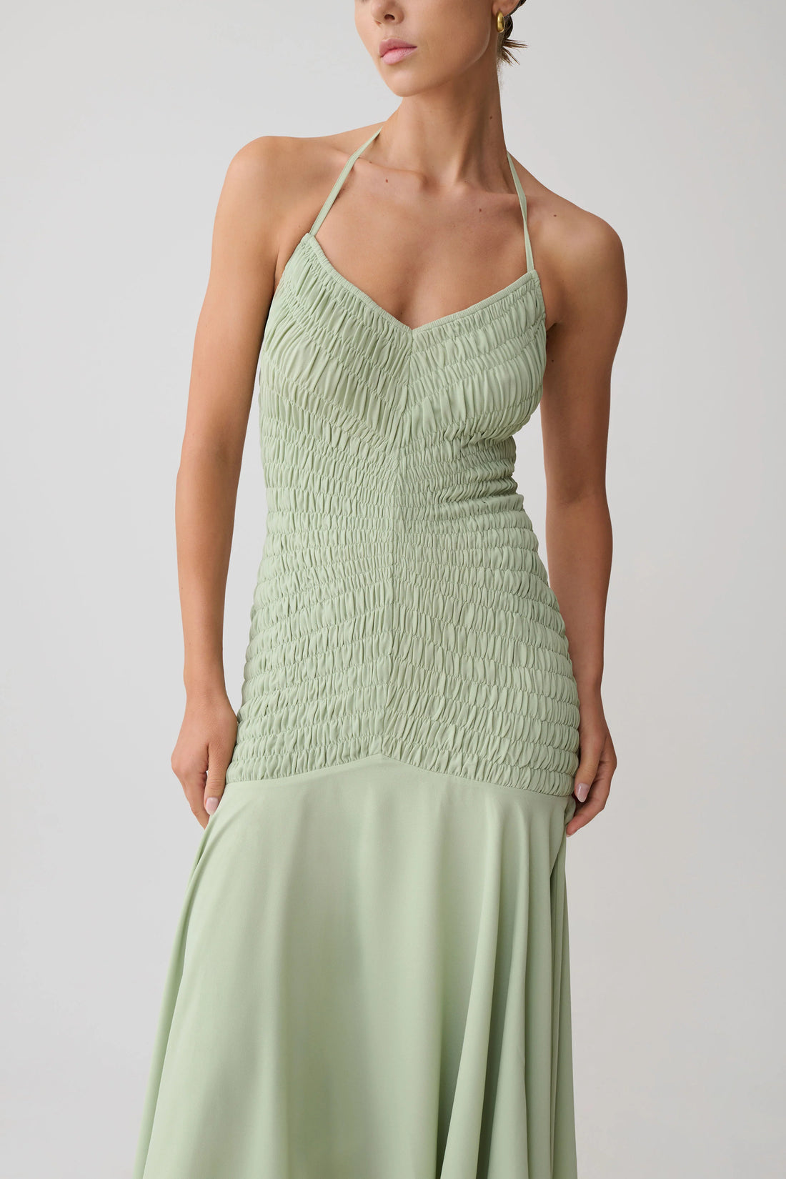 Woman wearing pale green halterneck maxi dress with shirred bodice and asymmetrical hem — Meshki | Endless UAE