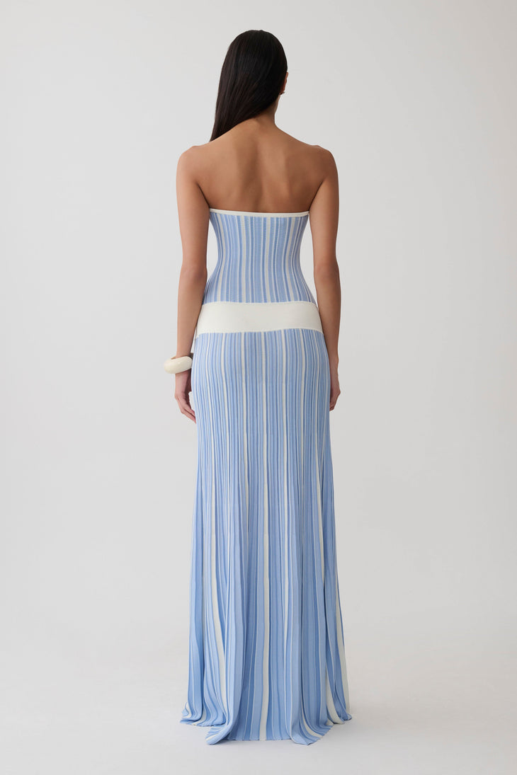 Woman wearing light blue striped strapless maxi knit dress with cream belt and white clutch — Meshki | Endless UAE