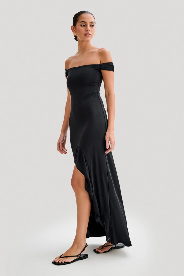 Woman wearing black off-shoulder slinky maxi dress with high-low hemline and gold hoop earrings — Meshki | Endless UAE