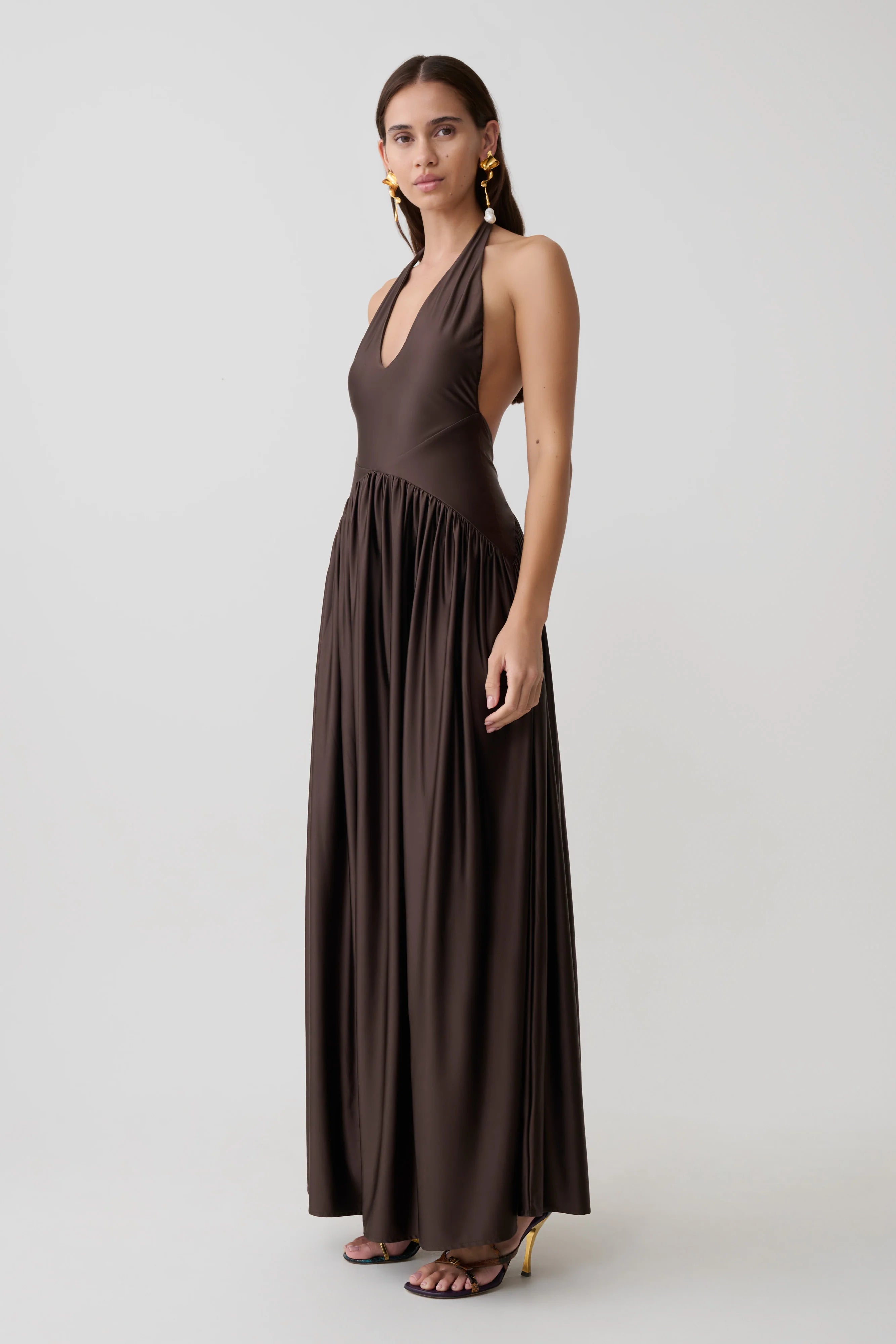 Woman wearing brown halter maxi dress with pleated skirt and gold heeled sandals — Meshki | Endless UAE