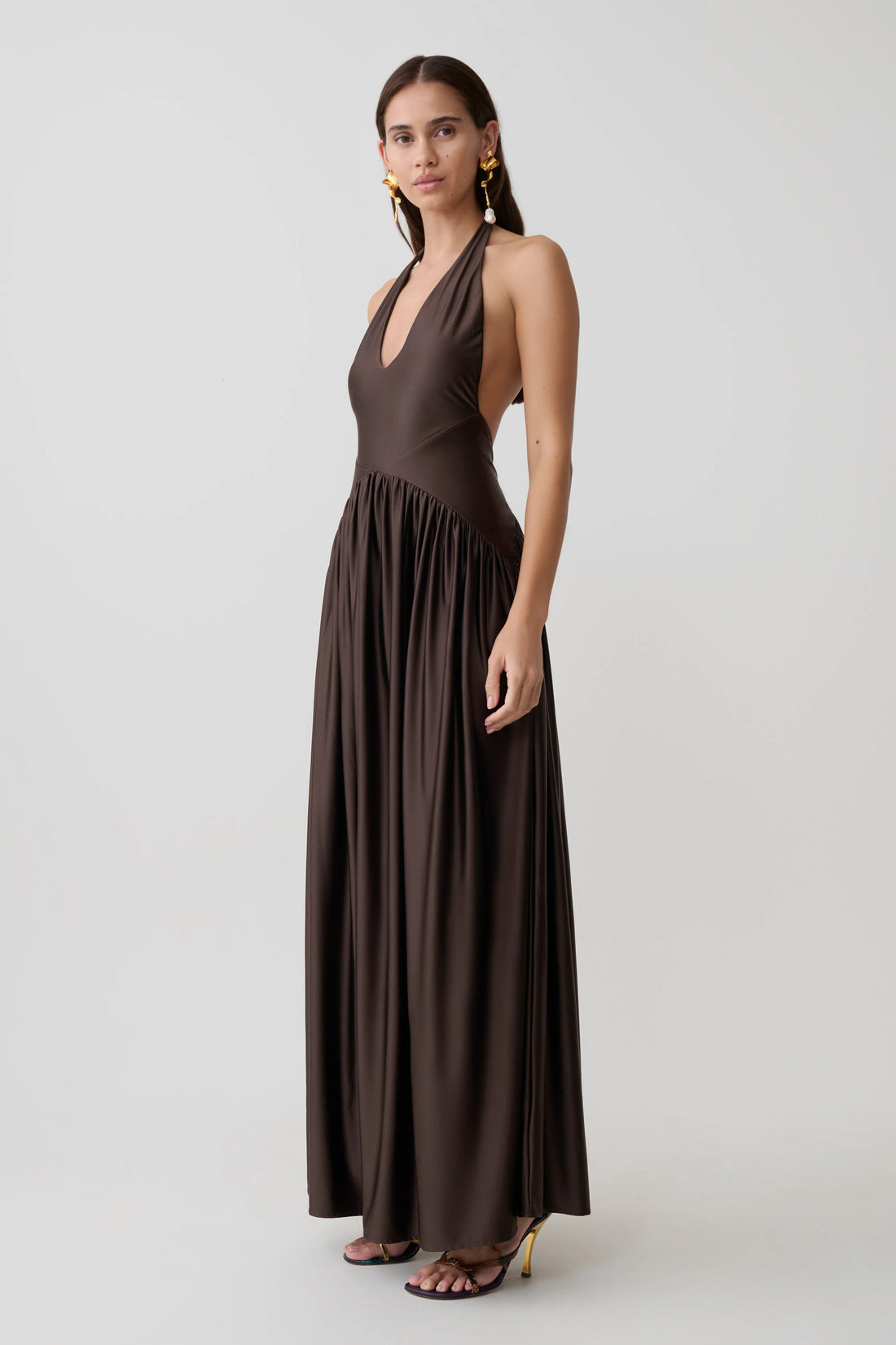 Woman wearing brown halter maxi dress with pleated skirt and gold heeled sandals — Meshki | Endless UAE