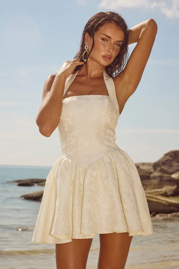 Sabine Mini Dress in cream with halter neckline and textured fabric on beach — Runaway The Label | Endless UAE