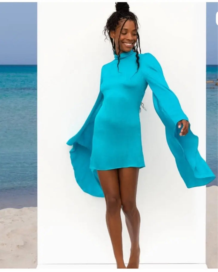 Woman wearing turquoise Farrah Dress with flowing cape sleeves at beach — Rat & Boa | Endless UAE