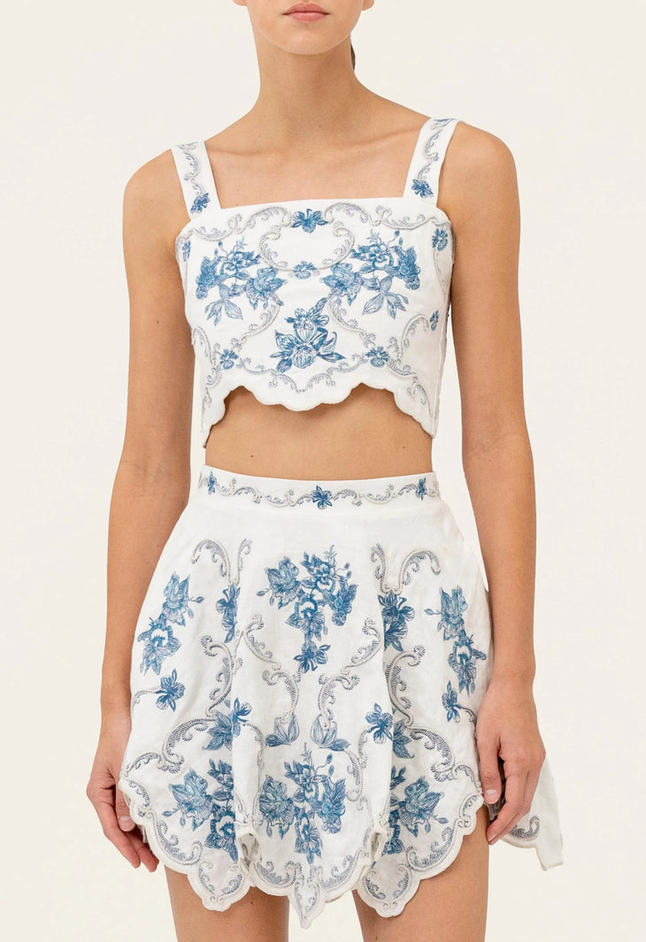 Woman wearing white cropped top and scalloped skirt with blue floral embroidery — Agua by Agua Bendita | Endless UAE