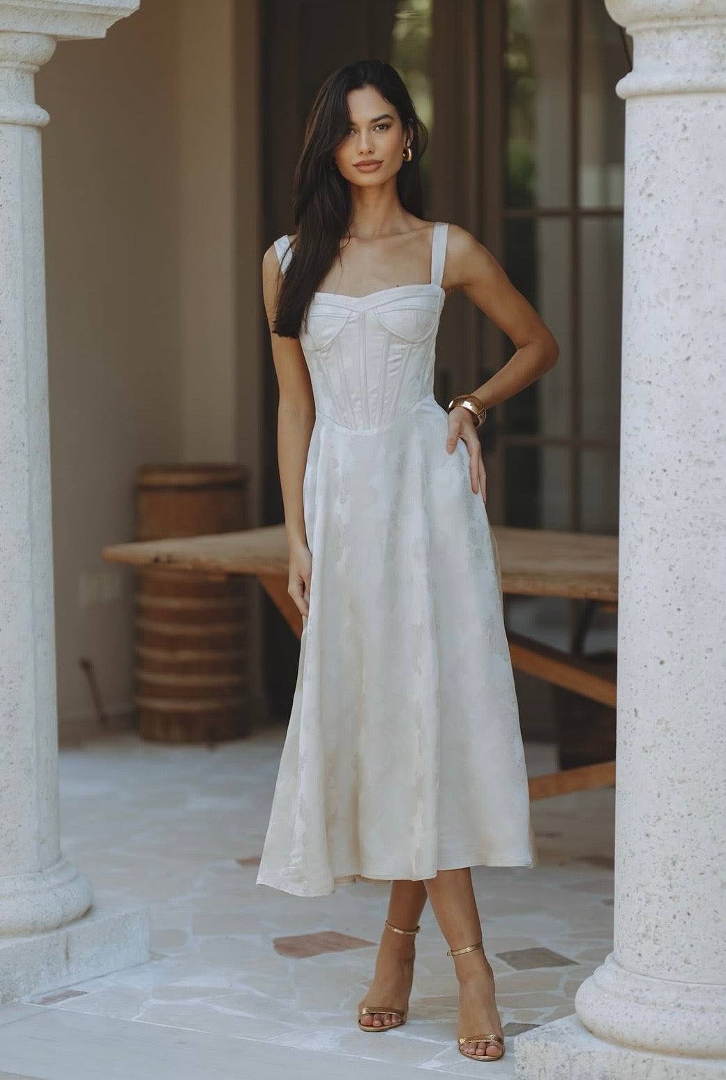 Woman wearing cream bustier midi dress standing between columns — Chic Le Frique | Endless UAE
