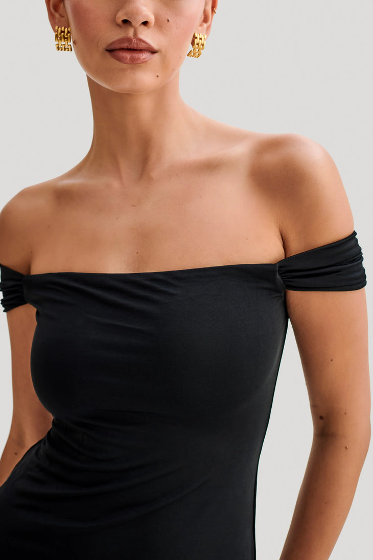 Woman wearing black off-shoulder slinky maxi dress with high-low hemline and gold hoop earrings — Meshki | Endless UAE