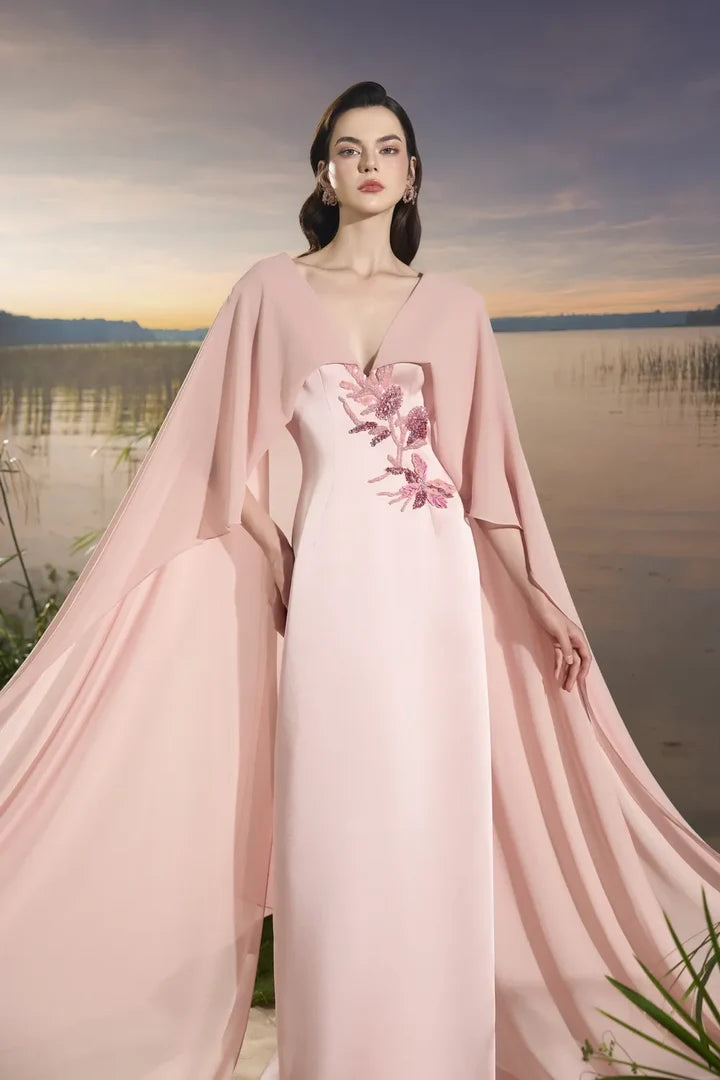 Woman wearing blush pink flowing gown with floral embellishment and draped cape at lakeside sunset — Tracy Studio | Endless UAE