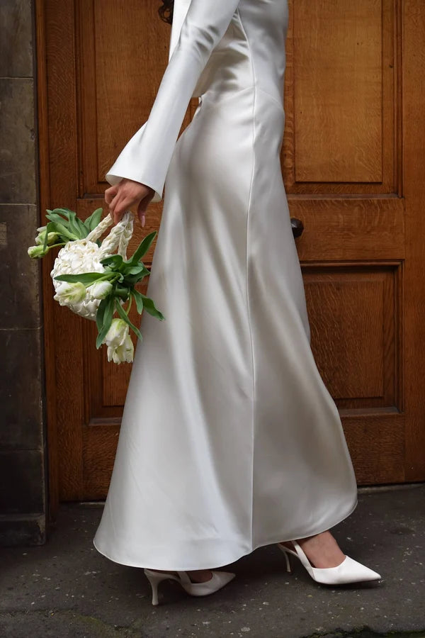 Bride in white satin Eden Dress holding white flowers — One Addington | Endless UAE