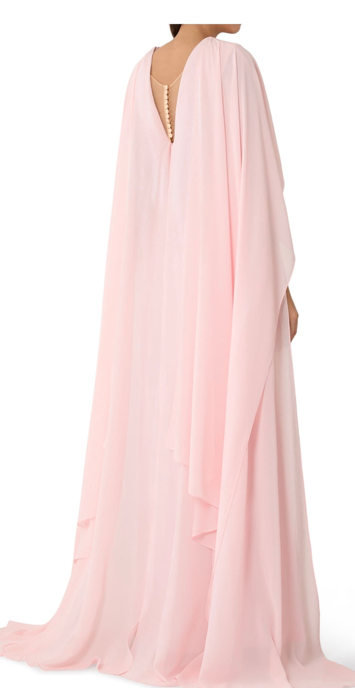 Woman wearing blush pink flowing gown with floral embellishment and draped cape at lakeside sunset — Tracy Studio | Endless UAE