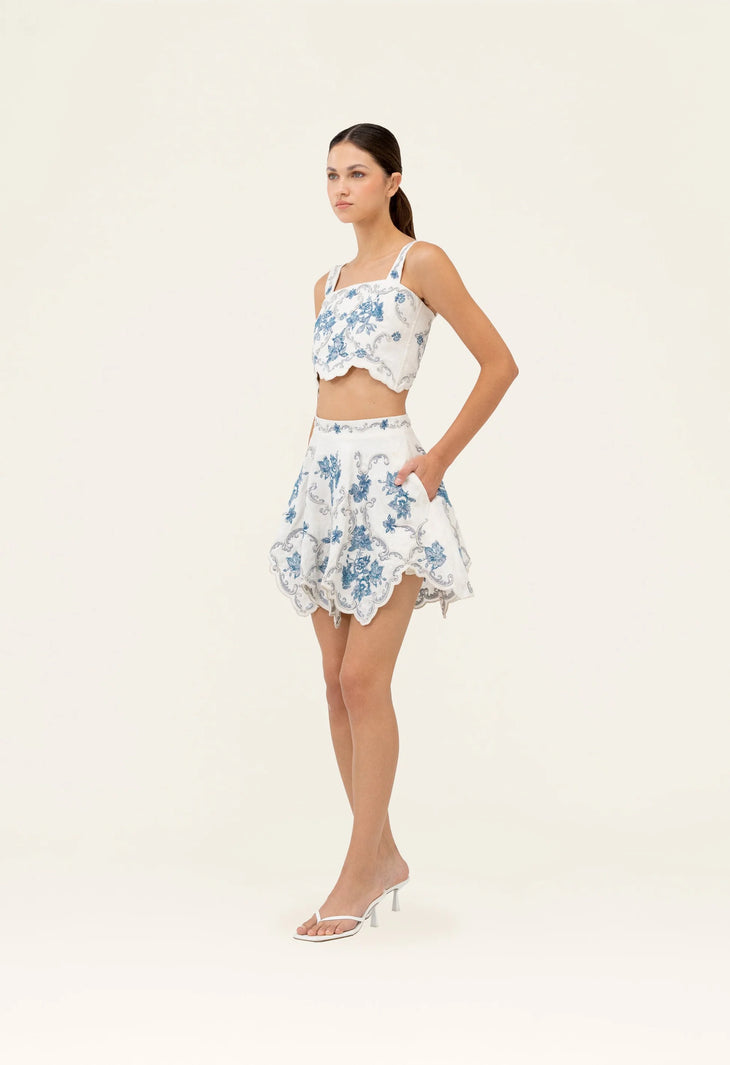 Woman wearing white cropped top and scalloped skirt with blue floral embroidery — Agua by Agua Bendita | Endless UAE