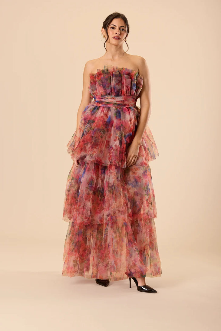 Woman wearing a strapless floral tulle maxi dress with tiered ruffle layers in red and pink tones — Lace & Beads | Endless UAE