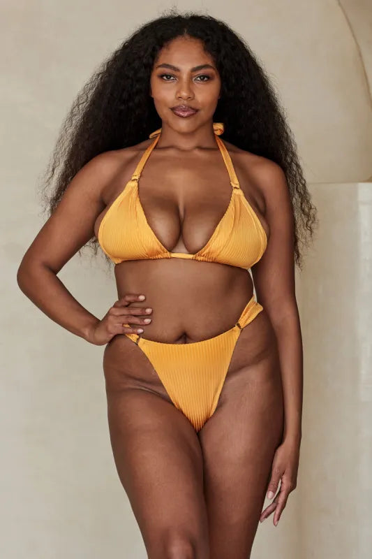 Woman wearing Clementine Wide Rib Bikini Set in golden yellow on beach with straw hat — Monday Swimwear | Endless UAE