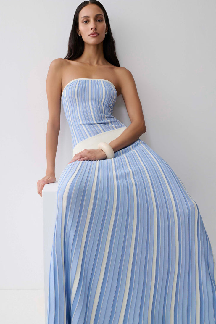 Woman wearing light blue striped strapless maxi knit dress with cream belt and white clutch — Meshki | Endless UAE