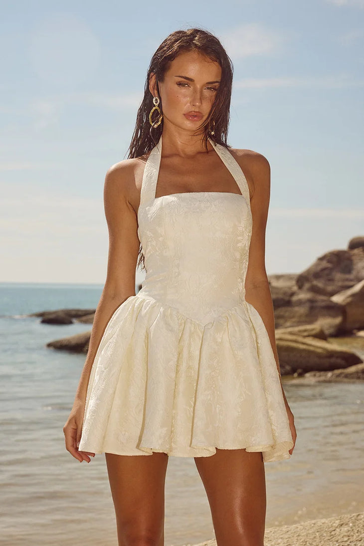 Sabine Mini Dress in cream with halter neckline and textured fabric on beach — Runaway The Label | Endless UAE