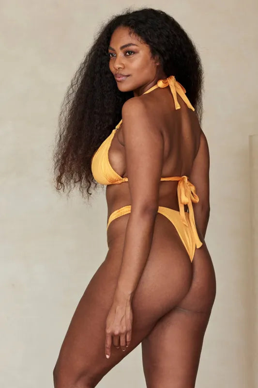 Woman wearing Clementine Wide Rib Bikini Set in golden yellow on beach with straw hat — Monday Swimwear | Endless UAE