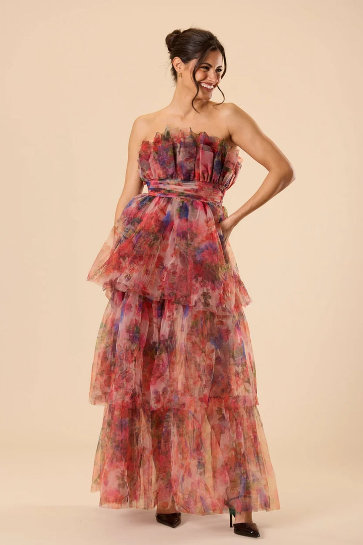 Woman wearing a strapless floral tulle maxi dress with tiered ruffle layers in red and pink tones — Lace & Beads | Endless UAE