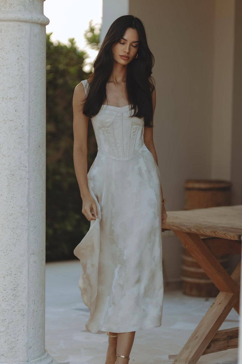 Woman wearing cream bustier midi dress standing between columns — Chic Le Frique | Endless UAE