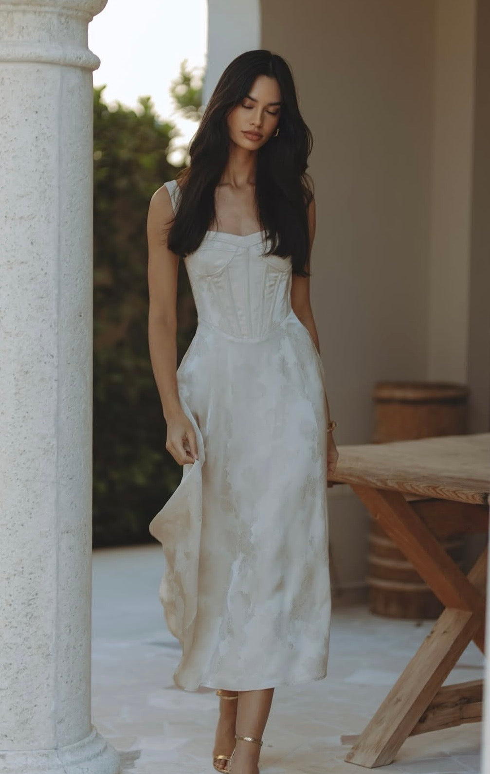 Woman wearing cream bustier midi dress standing between columns — Chic Le Frique | Endless UAE