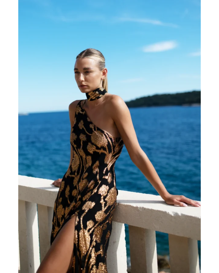 Woman wearing black and gold patterned halter dress by white railing overlooking blue ocean — Alexandra Miro | Endless UAE