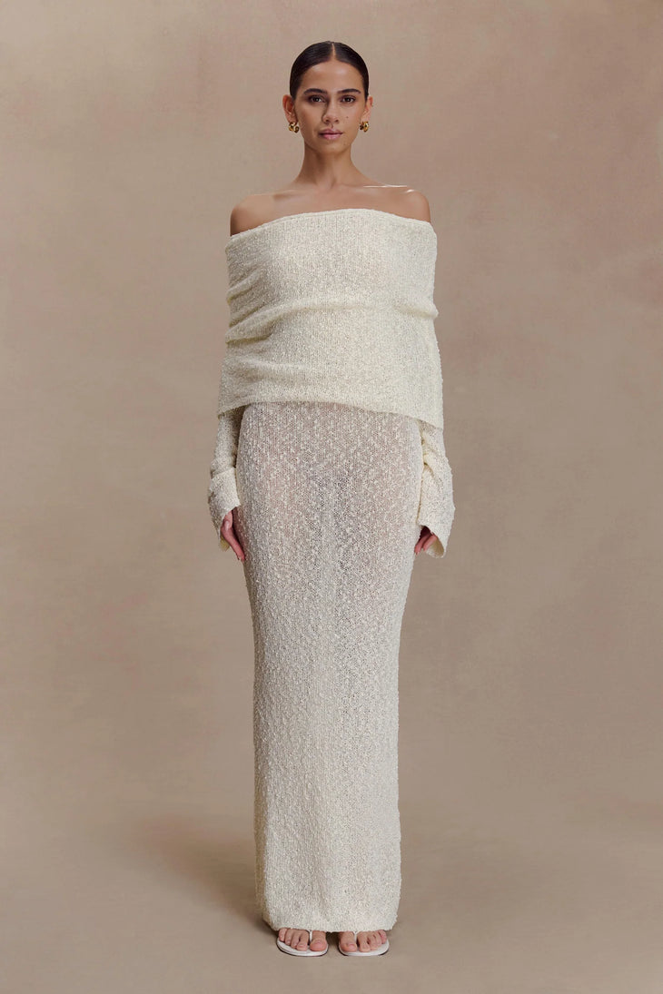 Woman wearing cream off-shoulder boucle maxi dress with draped sleeves and gold woven handbag — Meshki | Endless UAE