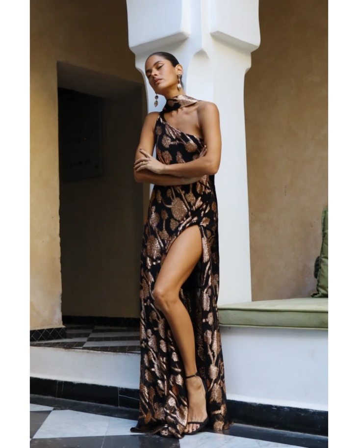 Woman wearing black and gold patterned halter dress by white railing overlooking blue ocean — Alexandra Miro | Endless UAE