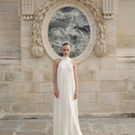 Woman wearing white flowing halter neck maxi dress standing in front of ornate stone archway — Nora The Label | Endless UAE