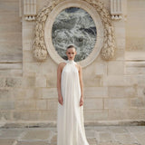 Woman wearing white flowing halter neck maxi dress standing in front of ornate stone archway — Nora The Label | Endless UAE