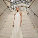 Elegant white halter neck maxi dress on model standing on Parisian staircase — Nora The Label | Endless UAE