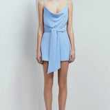 Cornflower blue cowl neck mini playsuit with tie waist detail and thin straps on model with strappy heels — Keepsake The Label | Endless UAE