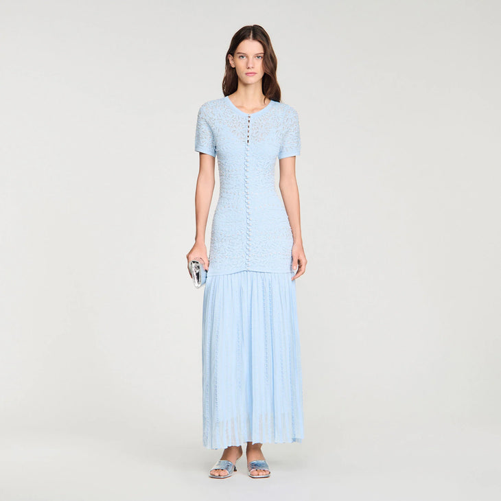 Woman wearing light blue textured knit maxi dress with button front detail and pleated skirt, paired with blue heeled sandals — Sandro | Endless UAE