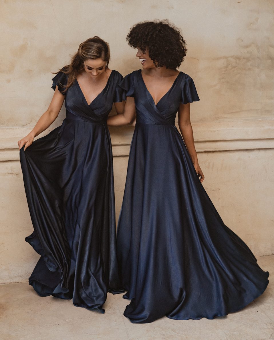 Two women in navy blue floor-length bridesmaid dresses with flutter sleeves and V-necklines — You&I Bridal | Endless UAE