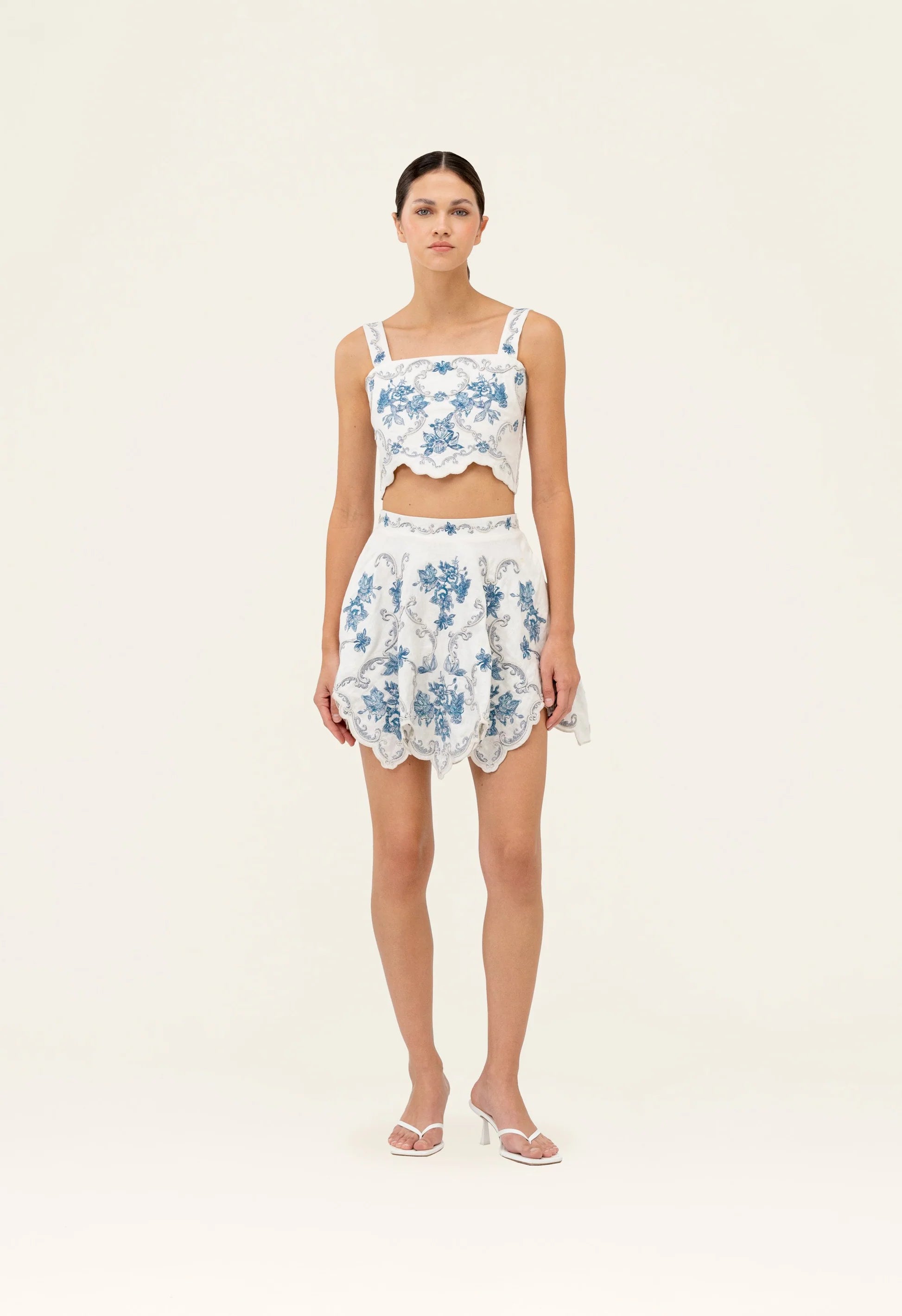 Woman wearing white cropped top and scalloped skirt with blue floral embroidery — Agua by Agua Bendita | Endless UAE