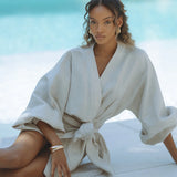 Woman wearing cream linen wrap mini dress with flutter sleeves by poolside — Chic Le Frique | Endless UAE