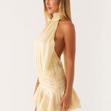 Woman wearing a pale yellow halter neck mini dress with pleated details and ruffle skirt, side view — Peppermayo | Endless UAE