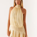 Woman wearing a pale yellow halter neck mini dress with pleated waist detail and ruffled hem — Peppermayo | Endless UAE