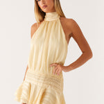 Blonde woman wearing cream yellow halter neck chiffon mini dress with pleated ruffles and high neckline — Peppermayo | Endless UAE
