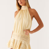 Blonde woman wearing cream yellow halter neck chiffon mini dress with pleated ruffles and high neckline — Peppermayo | Endless UAE