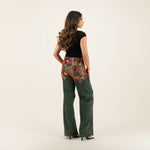 Woman wearing green wide-leg denim jeans with colorful patchwork belt detail and black top, viewed from behind — Quab | Endless UAE