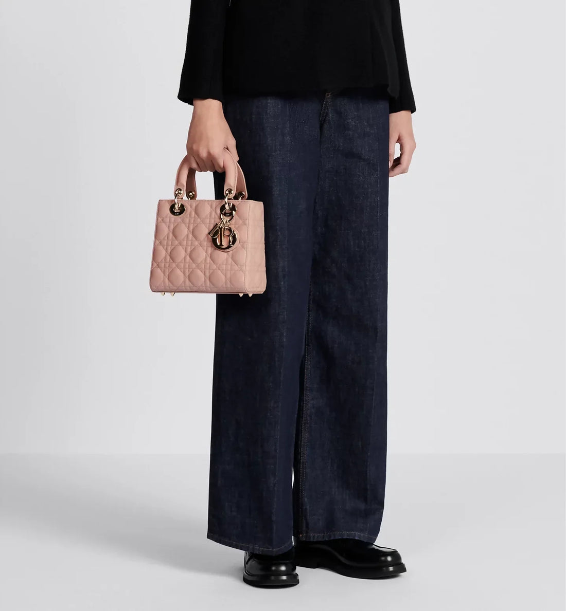 Small pink quilted Lady Dior bag with gold-tone hardware and charm, held by model wearing navy wide-leg pants — Christian Dior | Endless UAE